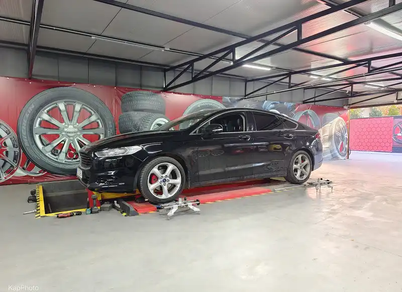 Un Ford Mondeo negru pe elevatorul de geometrie, cu peretele pictat cu roți.