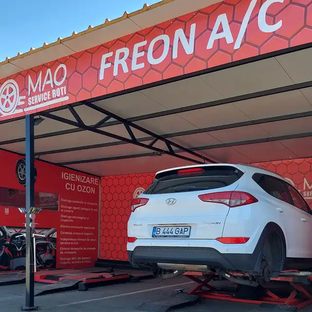 Un SUV alb ridicat sub copertina roșie cu scrisul Freon A/C.