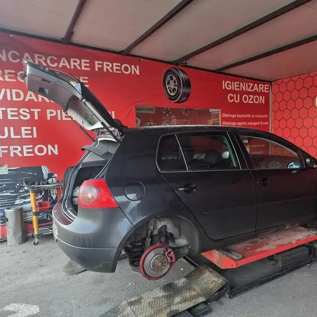 Un Volkswagen Golf fără roți, sub peretele cu Încărcare freon, Vidare și Test pierderi.