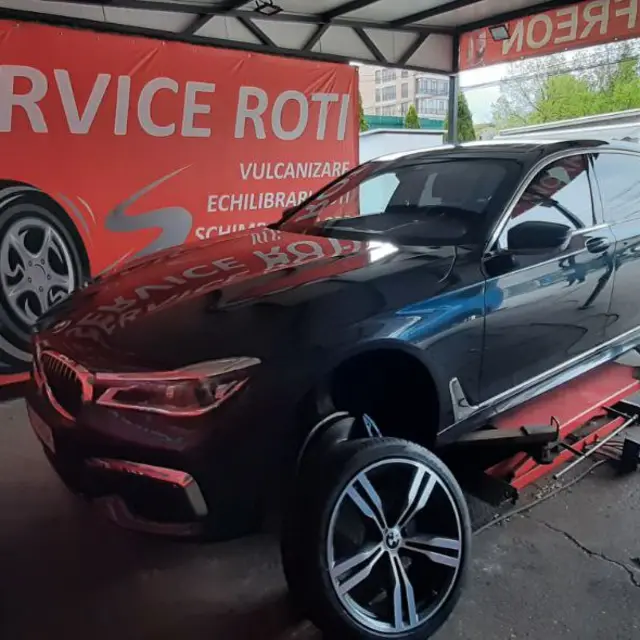 Un BMW negru pe elevator, cu roțile scoase, sub panoul Service roți.